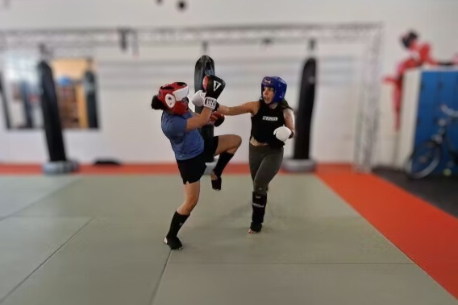 Two ladies sparring ART Boxing wearing full protection gear. Head gear, shin guards and boxing gloves.